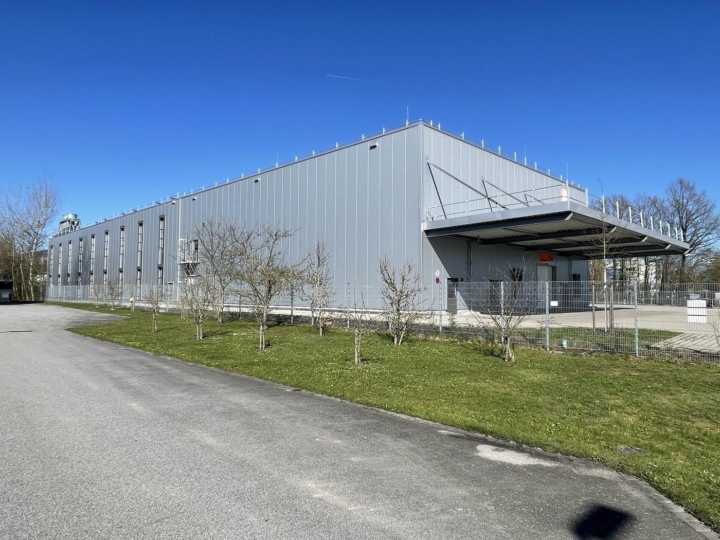 Lange graue Hallenfassade mit Lichtbändern und großem Vordach über der Andienung